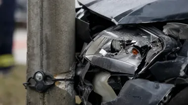 Rozbite przednie zderzenie i reflektor czarnego samochodu po uderzeniu w betonowy słup.